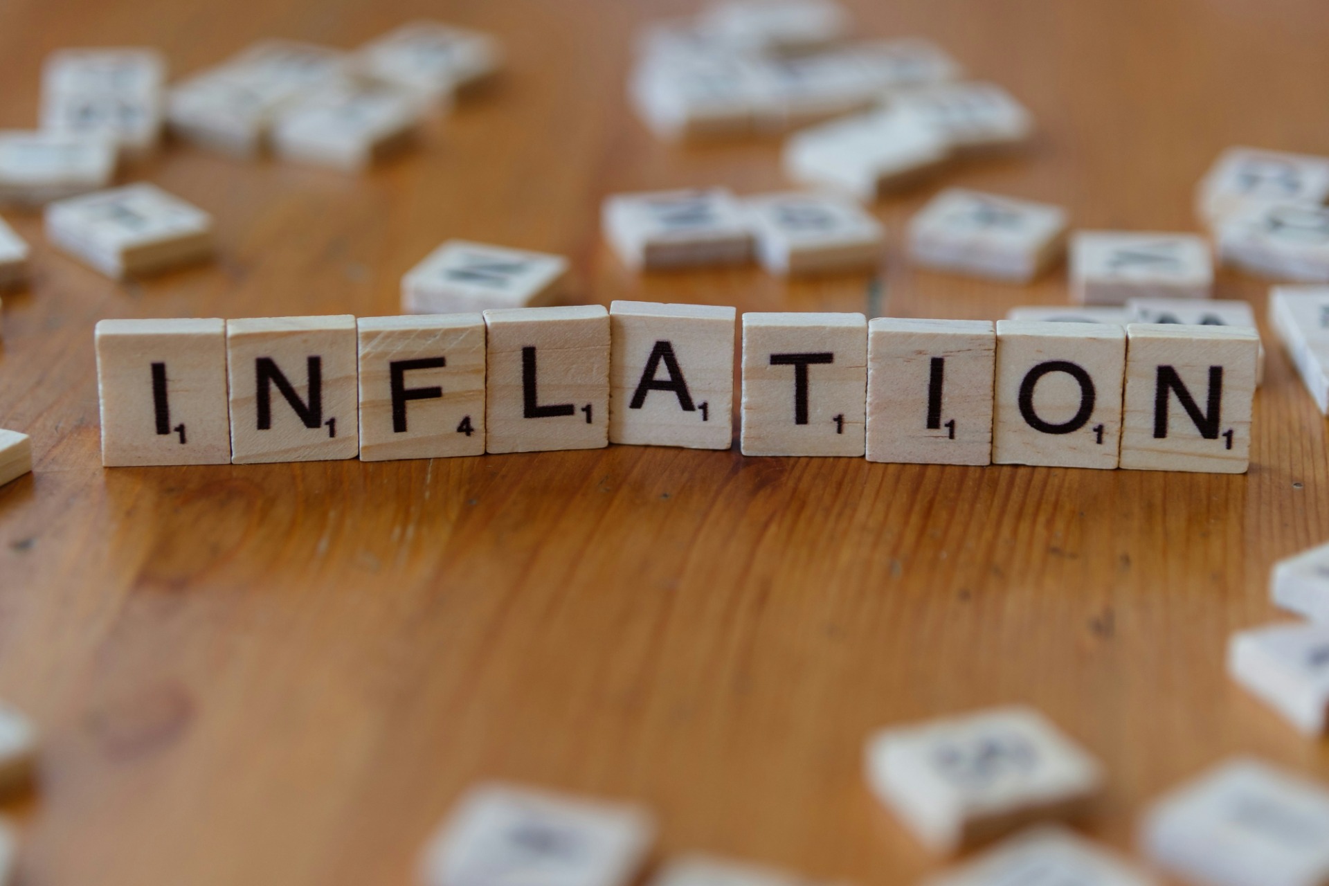 Blocos de madeira com letras formando “INFLATION”, em fila sobre mesa de madeira, fundo desfocado.